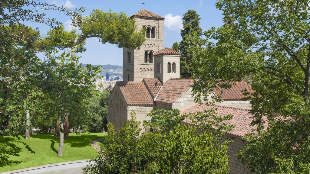 푸른 하늘 아래 녹음, 나무, 언덕으로 둘러싸인 붉은 기와 지붕이 있는 석조 교회.