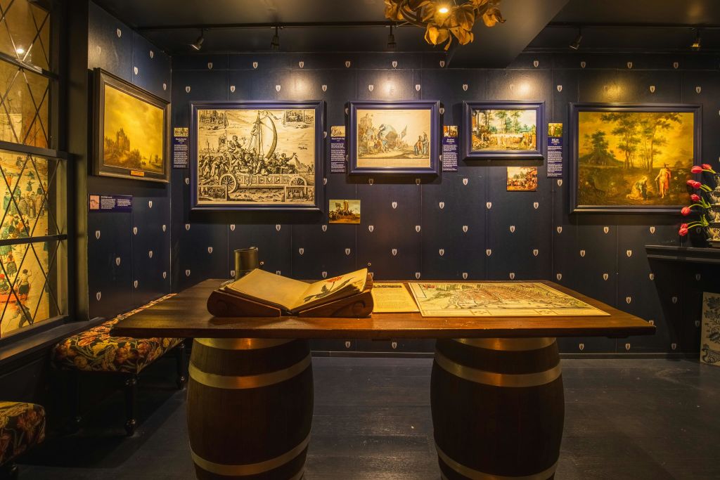 어두운 벽에 그림이 그려진 박물관 전시와 나무 통에 열린 책이 다리로 놓인 테이블이 있습니다.