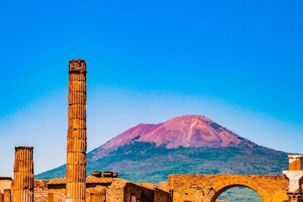 맑고 푸른 하늘 아래 산을 배경으로 기둥과 아치가 있는 고대 유적지.