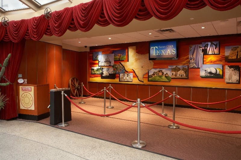 텍사스 랜드마크, 레드 벨벳 커튼, 빨간 밧줄이 달린 지점의 이미지가 담긴 "텍사스 너머의 하늘" 이라는 제목의 전시물입니다.