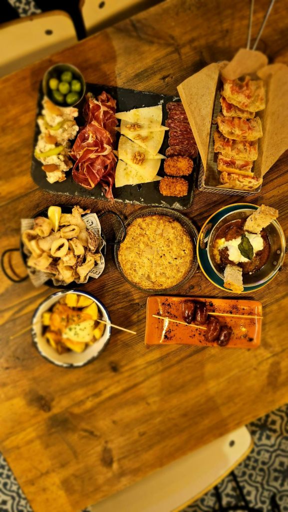 경화 고기, 치즈, 칼라마리 튀김, 크로켓, 감자, 나무 테이블에 구운 물건을 포함한 다양한 타파스 요리.