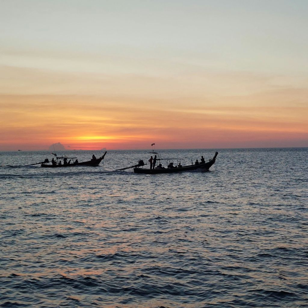 오렌지색과 분홍색 하늘색의 석양의 바다에서 보트의 실루엣.