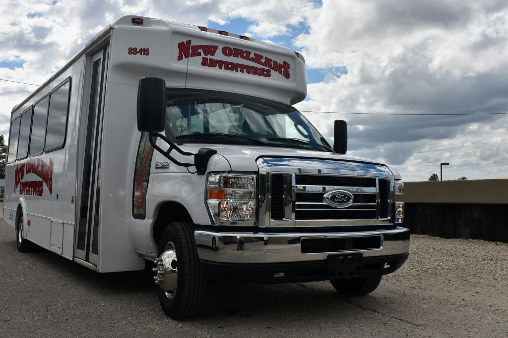 상단에 "뉴올리언스 어드벤처" 라고 쓰여진 흰색 투어 버스가 흐린 하늘 아래 주차되어 있습니다.