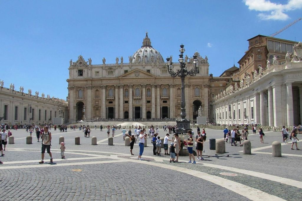 맑고 푸른 하늘 아래 성 베드로 대성당을 배경으로 성 베드로 광장을 걷고 모이는 관광객들.