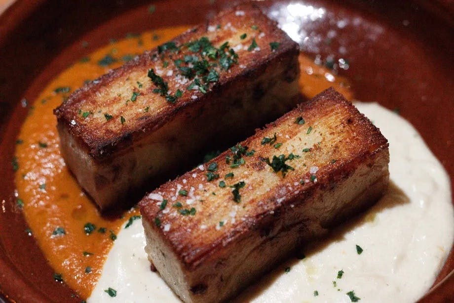 허브로 장식된 직사각형 구운 고기 두 조각을 크림색의 화이트 소스와 적갈색 베이스에 담았습니다.