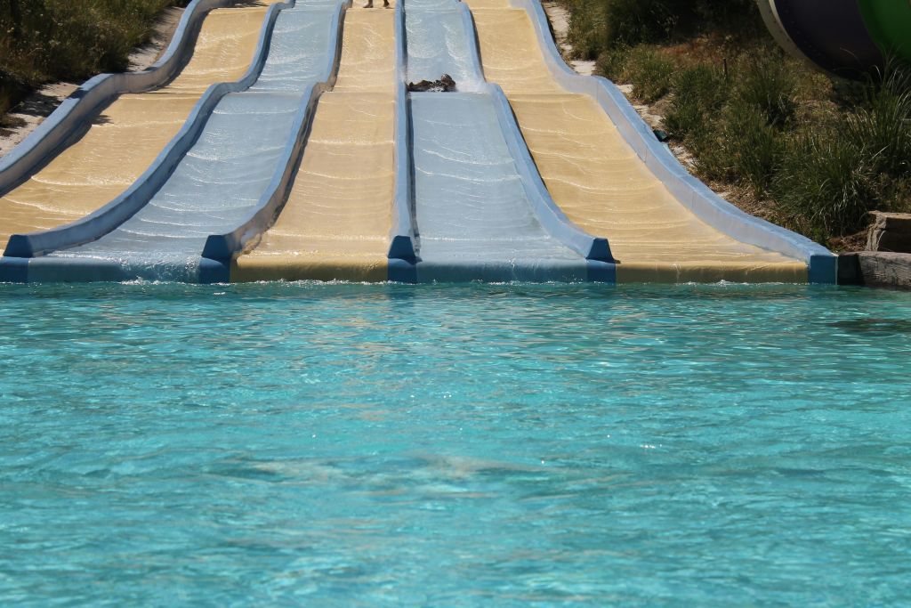 3 개의 워터 슬라이드가 활기찬 푸른 수영장으로 이어지고 양쪽에 녹지가 있습니다.