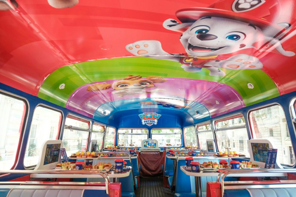 다채로운 Paw Patrol 장식이 있는 테마 버스의 내부에는 식탁, 파란색 좌석, 음식 디스플레이가 설치되어 있습니다.