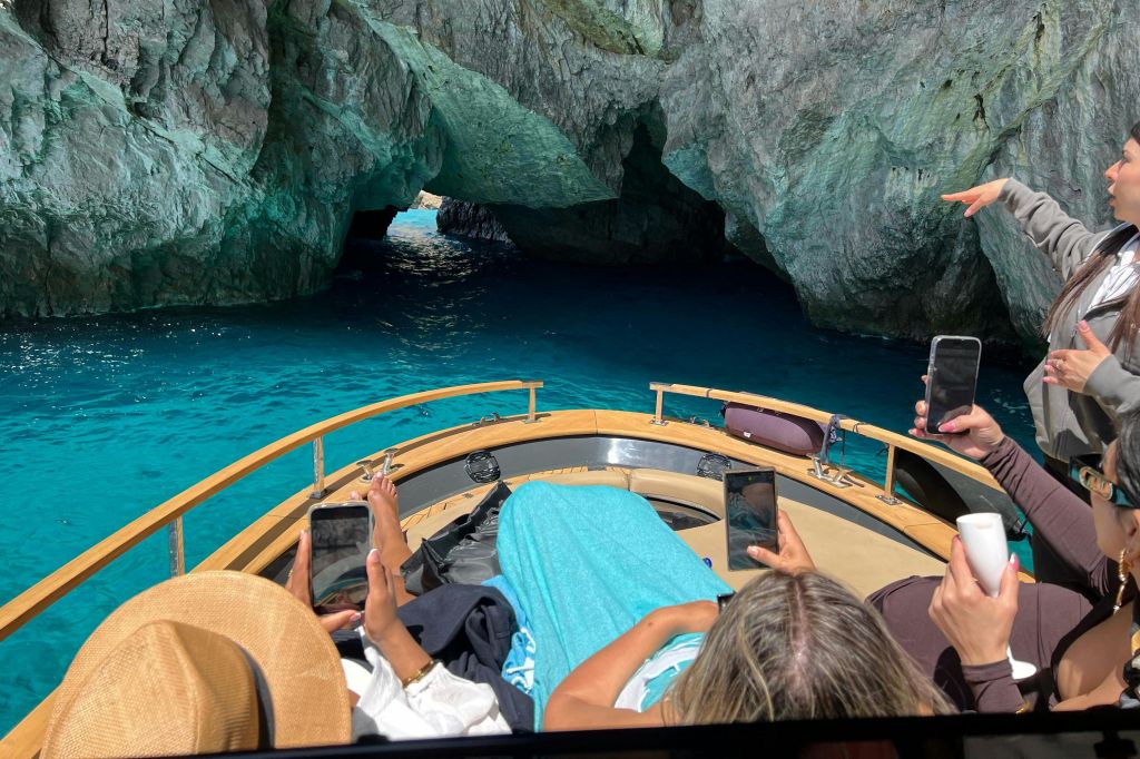 보트를 타고 청록색 물과 바위 동굴을 배경으로 사진을 찍는 사람들.