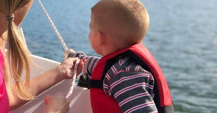 빨간 구명조끼를 입은 어린 아이가 보트에 밧줄을 매고 있고, 배를 배경으로 물이 보입니다.