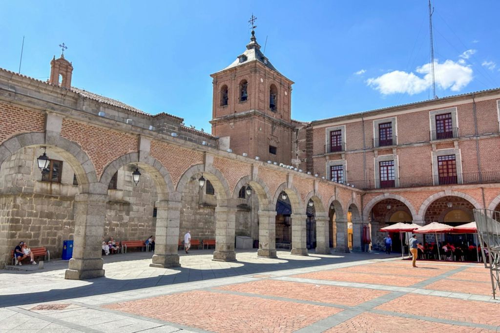 맑고 푸른 하늘 아래 석조 아치와 붉은 벽돌 건물, 종탑이 있는 마당.