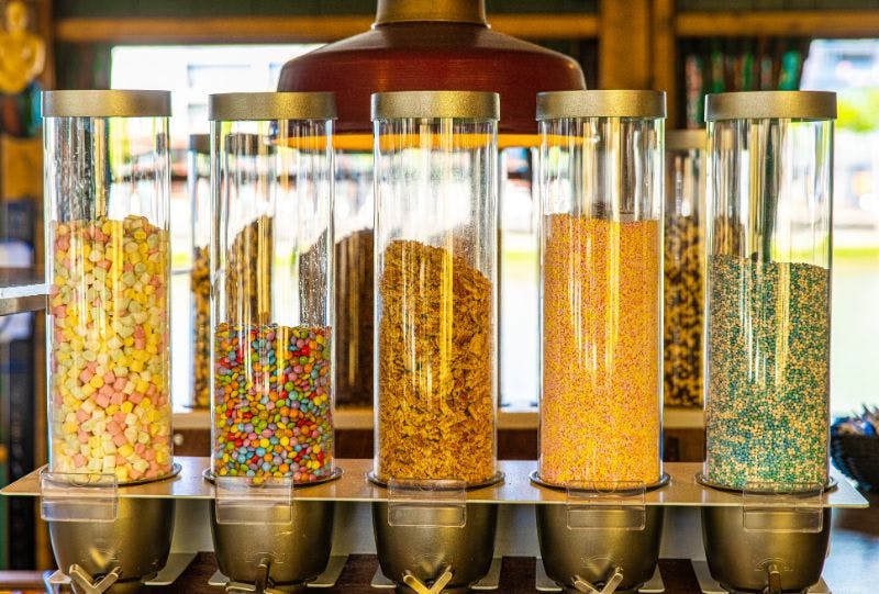 다양한 시리얼과 다채로운 토핑으로 채워진 투명 디스펜서에는 각각 하단에 은색 손잡이가 장착되어 있습니다.