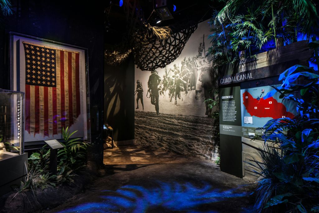 미국 국기, 전장에 있는 군인들의 벽 사진, 유물 전시, 과달카날에 대한 정보 패널을 전시하는 박물관 전시물입니다.