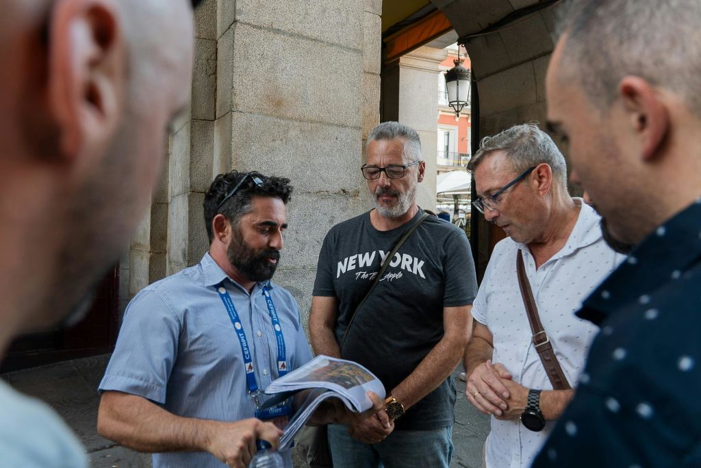 건물과 전등 기둥을 배경으로 4명의 남성이 서류나 지도를 보며 바깥에 서 있습니다.