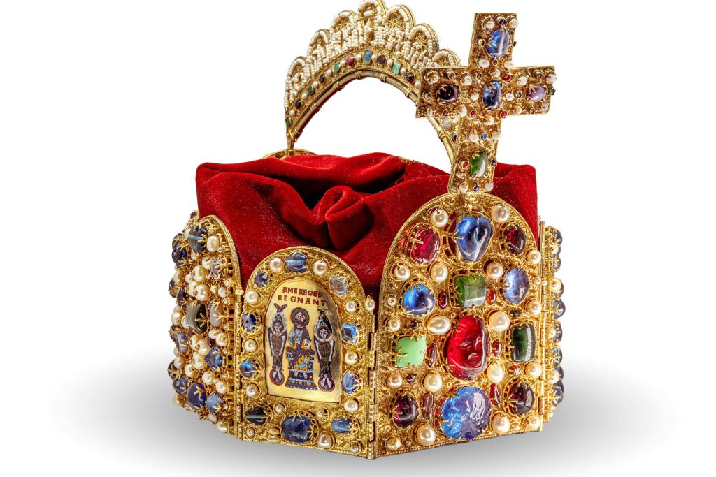 정교한 디자인과 종교적 이미지가 특징인 십자가가 있는 보석으로 장식된 금색 왕관으로 내부에 빨간색 천으로 채워져 있습니다.