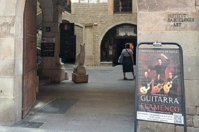 오래된 석조 건물을 배경으로 플라멩코 기타 콘서트를 광고하는 표지판 근처의 안뜰을 걷고 있는 사람.