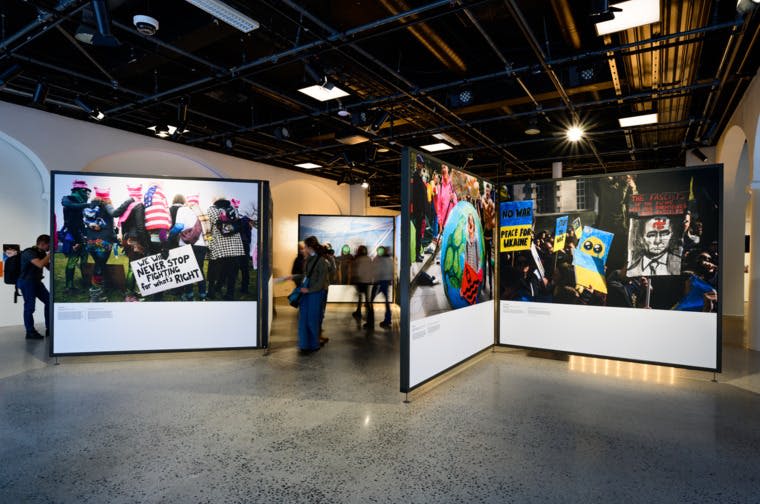 독립 패널에 대형 시위 사진이 전시된 실내 갤러리. 사람들이 전시회 사이를 걷고 있습니다.