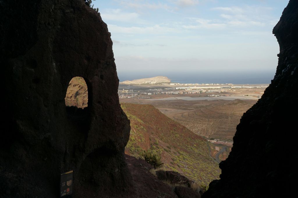 창문 같은 개구부가 있는 자연 암석 지층은 먼 해안 마을과 바다를 둘러싸고 있습니다.