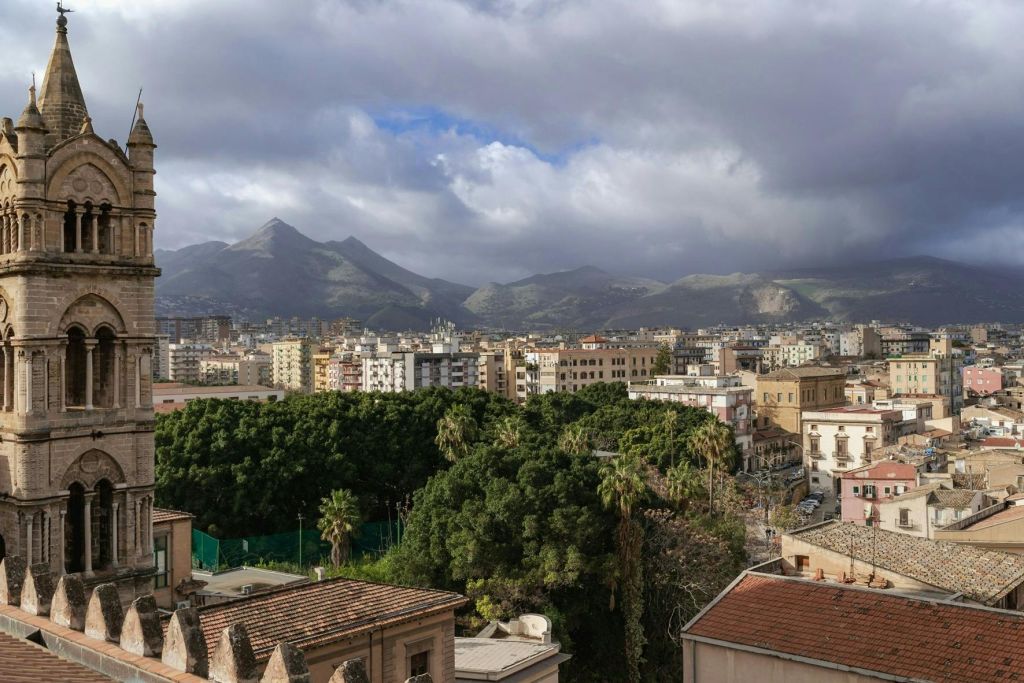 녹음이 우거진 도시 풍경과 전경의 건물, 흐린 하늘 아래를 배경으로 한 산.