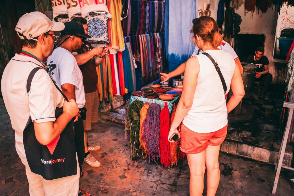 화려한 색상의 패브릭을 둘러보고 길거리 시장 노점에서 원사의 가죽을 걸고 있는 사람들. 한 사람이 사진을 찍고 있습니다.
