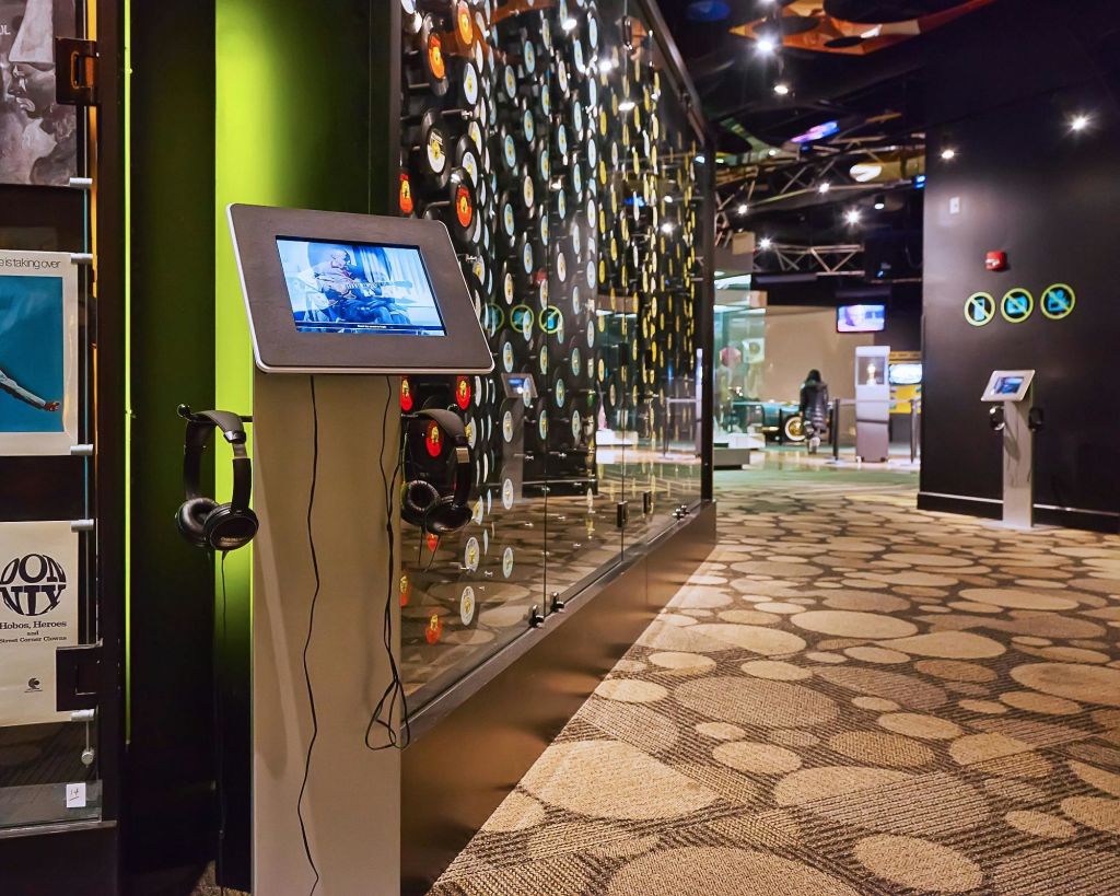 원형 패턴의 바닥, 벽에 기록물 전시, 대화형 터치스크린 스테이션이 있는 현대적인 박물관 전시관입니다.