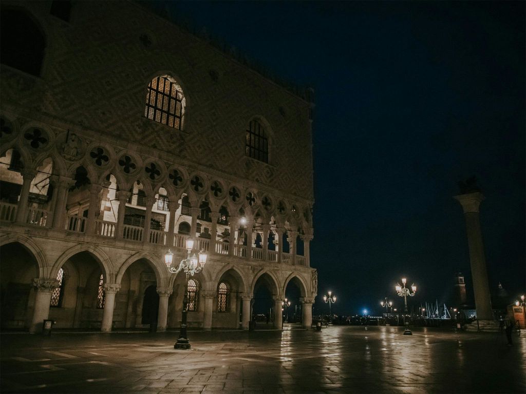 밤에는 아치형 창문과 기둥으로 역사적인 건물을 밝히고, 가로등은 빈 자갈 광장을 밝힙니다.