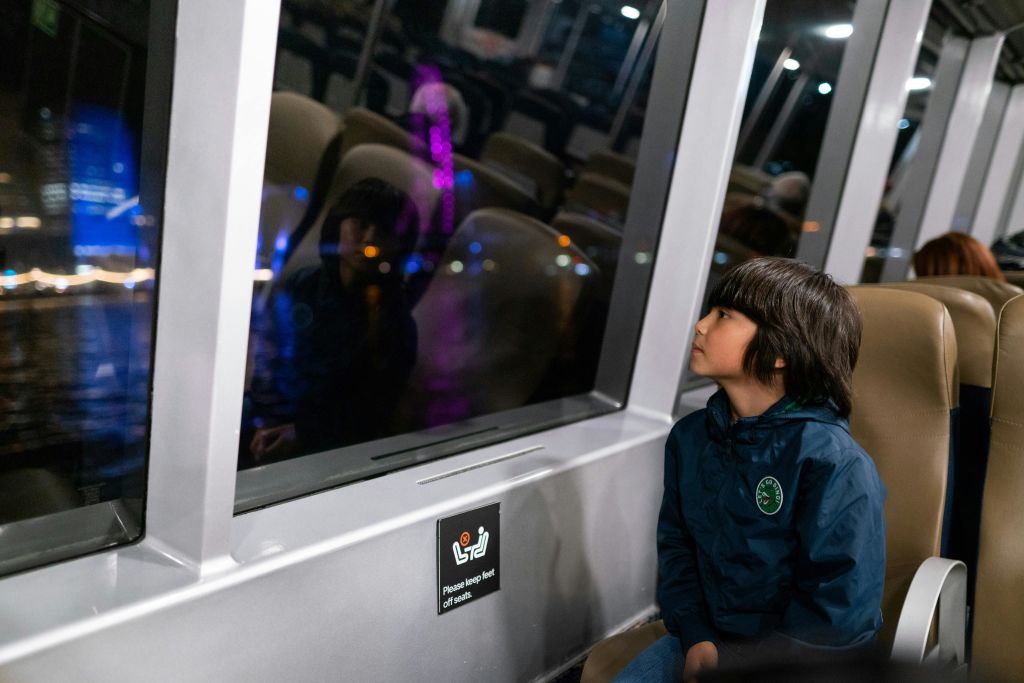 파란색 재킷을 입은 어린이가 밤에 기차에 앉아 창밖을 내다보고 있습니다.