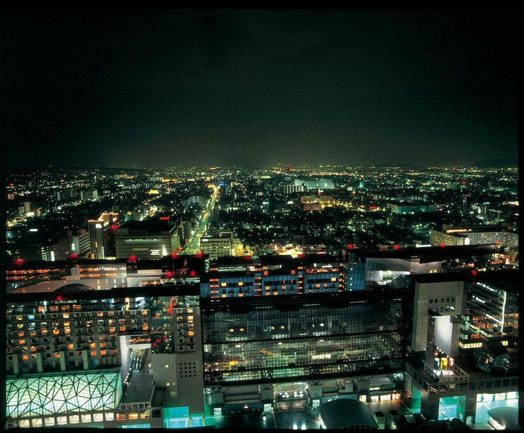 건물, 불빛이 들어오는 거리, 수평선을 향해 흩어져 있는 불빛이 어우러진 밤의 도시 풍경이 공중에서 펼쳐집니다.