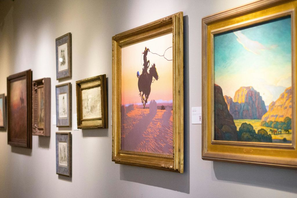 화려한 석양을 배경으로 카우보이가 말을 타고 있는 그림을 비롯해 액자에 담긴 작품을 전시하는 갤러리 벽면입니다.