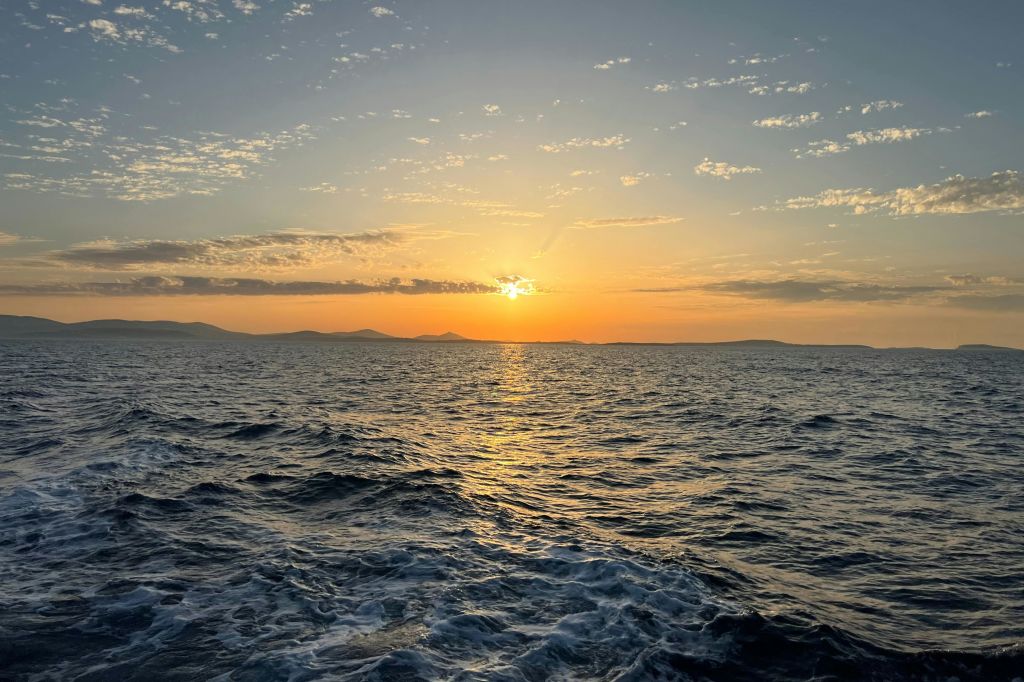 부드러운 파도와 흩날리는 구름과 지는 해가 특징인 활기찬 하늘과 함께 석양이 질 무렵 바다의 경치를 감상할 수 있습니다.