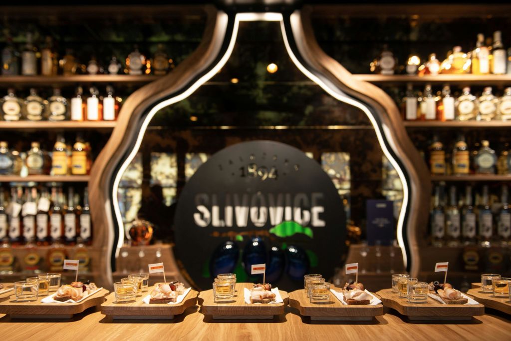 "Slivovice" 라고 쓰인 백라이트 표지판 앞에 도금된 간식과 음료를 갖춘 나무 바가 있습니다.