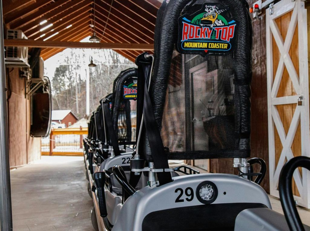 "Rocky Top Mountain Coaster" 라고 표시된 나무 캐노피 아래 롤러코스터 차량 시트백. 차량 번호가 표시됩니다.