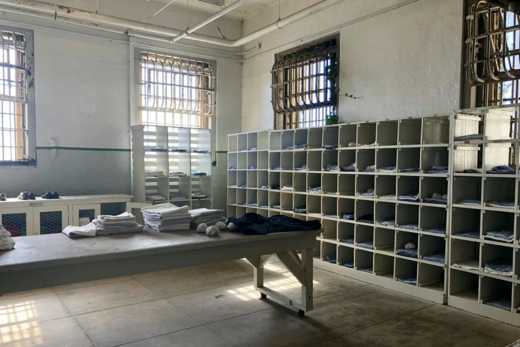 창문이 막힌 방, 접힌 옷 선반, 접힌 세탁물이 놓인 중앙 테이블, 입방체 구멍이 있는 벽.