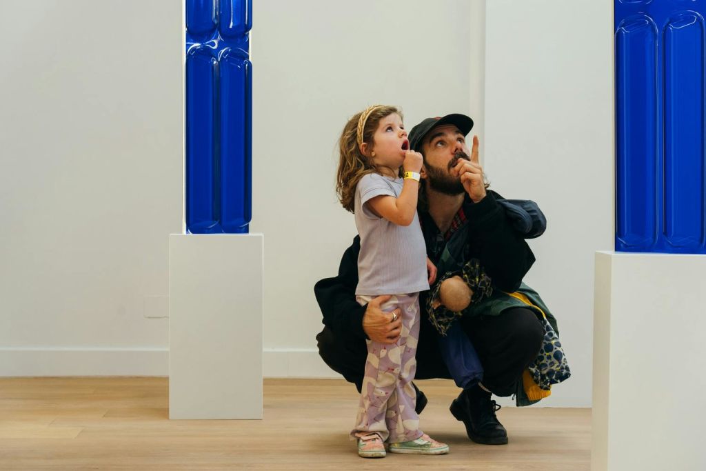 한 남자와 어린 소녀가 파란색 조각품이 전시된 미술관에서 무언가를 관찰하고 있습니다.