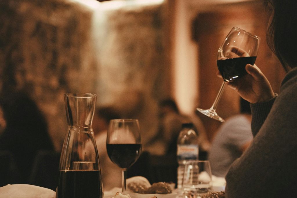 와인잔, 레드 와인 캐러피, 식탁에 놓인 물병, 와인잔을 배경으로 한 손.