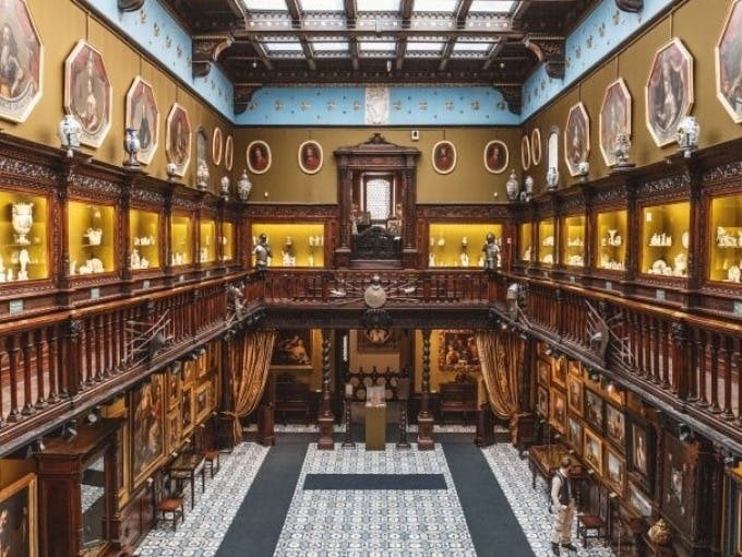 정교한 건축물, 두 층의 액자 초상화, 타일 바닥을 둘러싼 디스플레이 캐비닛을 갖춘 화려하고 유서 깊은 갤러리입니다.