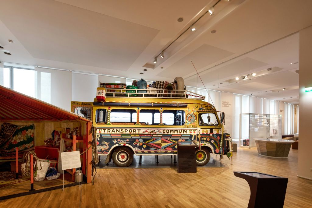 나무 바닥이 있는 밝은 조명으로 장식된 박물관 방에 전시된, 짐이 놓인 장식된 빈티지 버스입니다.