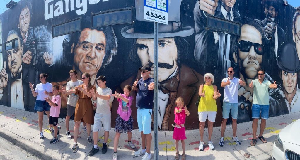 두 남자가 강렬한 표정을 짓고 있는 벽화 앞의 한 무리. 그들은 장난스럽게 포즈를 취하며 카메라를 가리키고 있습니다.