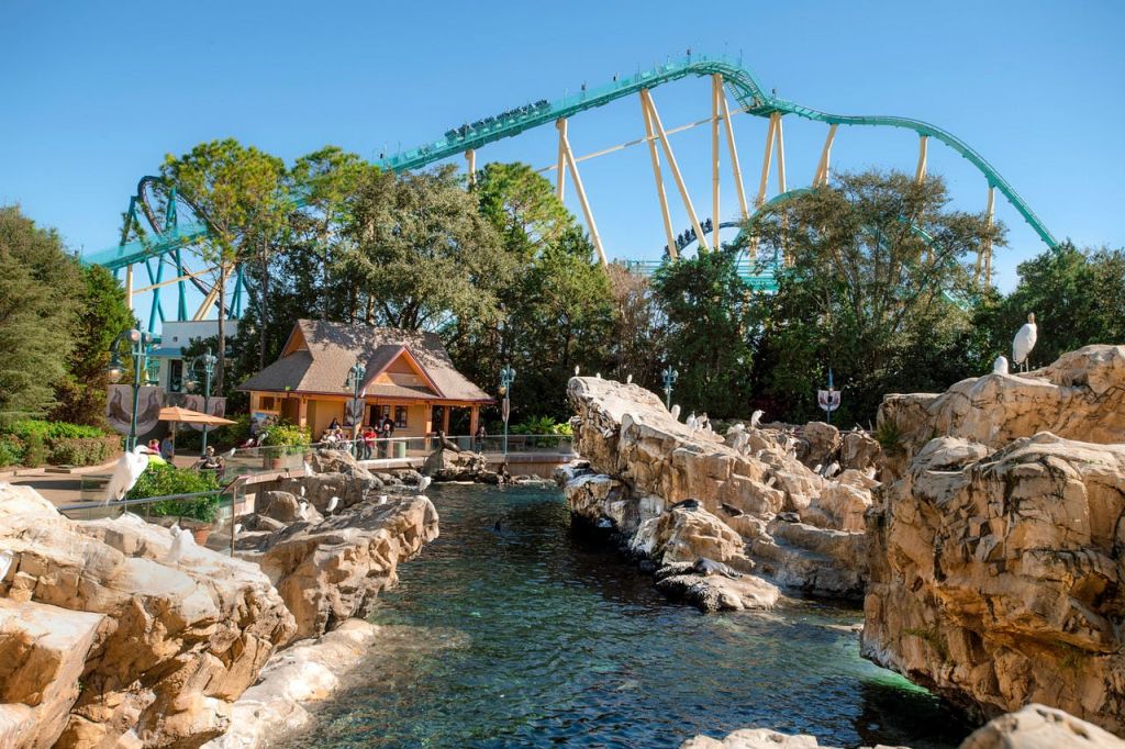 바위 물 위에 녹색 트랙이 있는 롤러코스터와 나무와 단풍으로 둘러싸인 작은 건물.