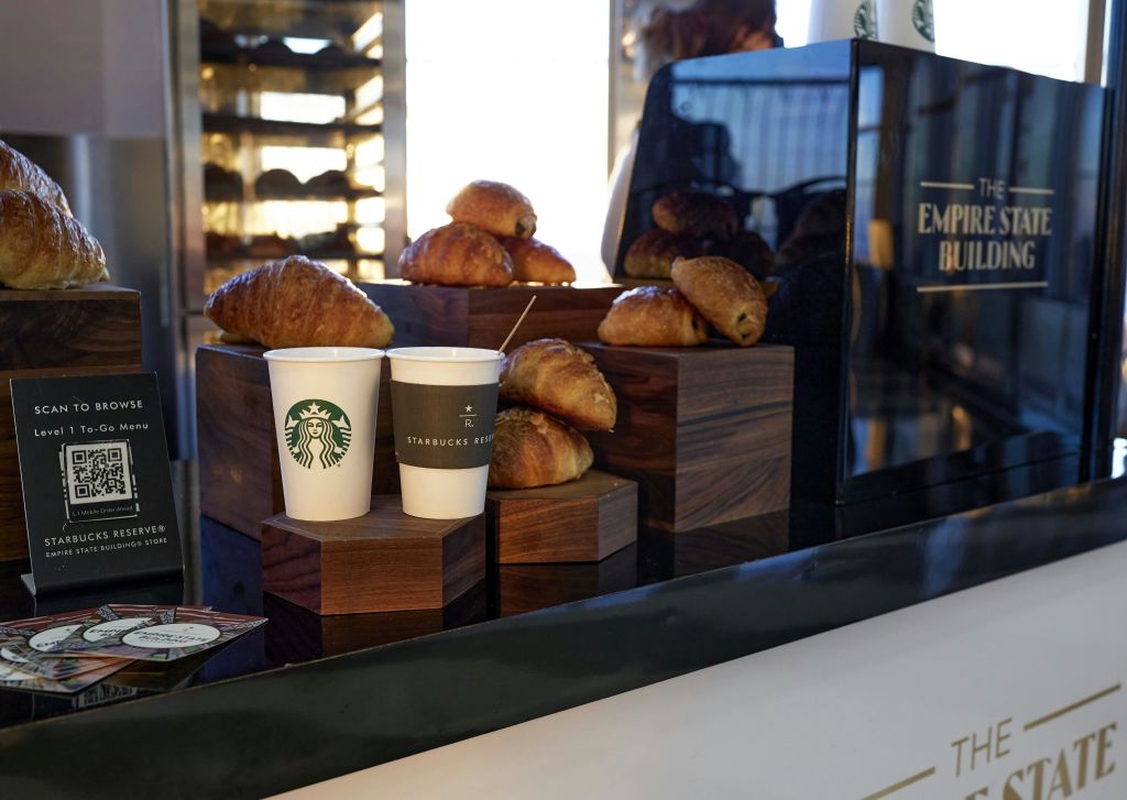 반사 표면과 베이커리 배경이 있는 카운터에 스타벅스 브랜드가 새겨진 크루아상과 컵 2개가 진열되어 있습니다.