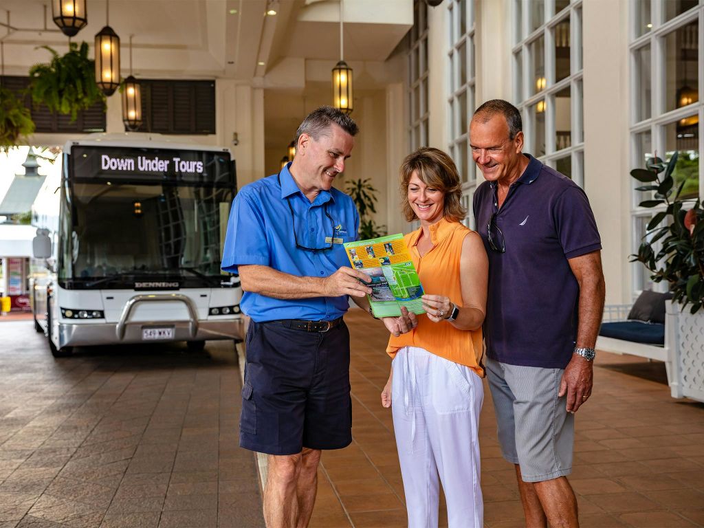 투어 가이드는 투어 버스 근처의 로비 공간에서 웃고 있는 커플에게 브로셔를 보여줍니다.