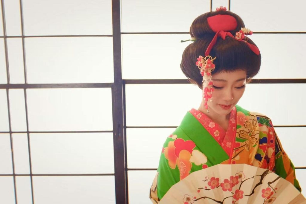 일본 전통 복장을 한 사람이 부채를 들고 쇼지 스크린 앞에 서 있습니다.