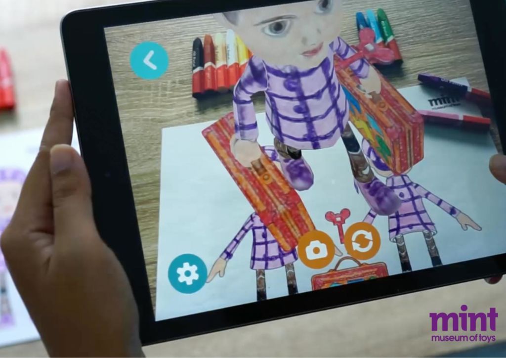 여행 가방을 들고 있는 어린이의 증강 현실 형상을 종이 그림 위에 표시하고 마커를 배경으로 한 태블릿.