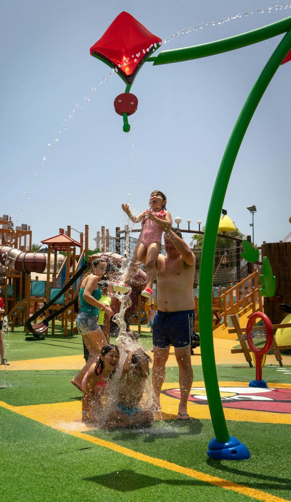 어린이와 성인은 등반 구조물과 미끄럼틀이 있는 활기찬 놀이터에서 물 뿌리기 놀이를 합니다.