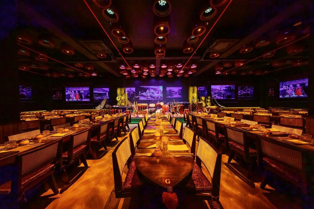 따뜻한 조명으로 조명이 켜진 긴 식탁이 있는 조명이 희미한 레스토랑입니다. 악기를 배경으로 한 보라색 무대.