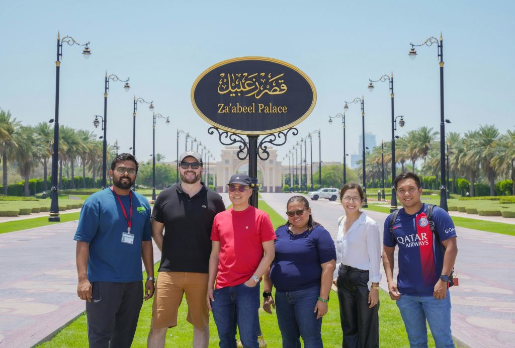 화창한 날, 야자수와 가로등을 배경으로 자빌 궁전 (Za 'abeel Palace) 표지판 앞에 5명이 서 있습니다.