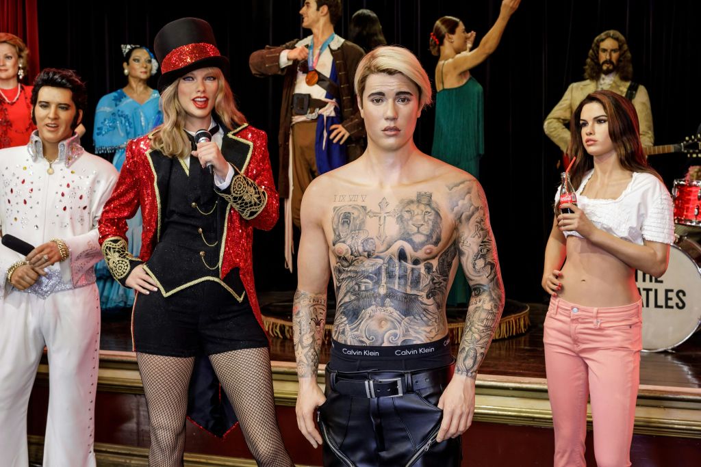 왁스 박물관의 인물: 문신을 한 남성, 반짝이는 빨간 재킷을 입은 여성, 음료를 들고 있는 분홍색 바지를 입은 또 다른 여성.