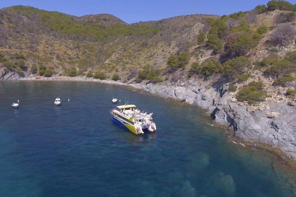 맑은 하늘 아래 바위 절벽과 푸른 언덕으로 둘러싸인 맑고 푸른 물이 흐르는 만의 쌍동선과 작은 보트.