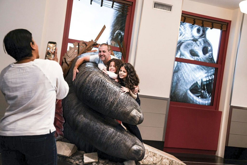 한 사람이 건물 내부에서 커다란 고릴라 손 조각을 들고 포즈를 취하고 있는 한 남자와 두 아이의 사진을 찍고 있습니다.