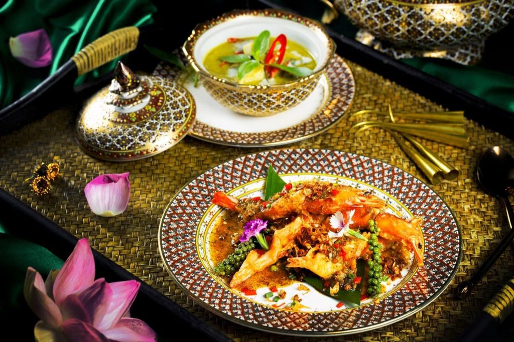 태국 음식으로 풍성하게 장식된 테이블 세팅으로, 화려한 그릇에 새우 요리와 수프가 담겨 있으며, 꽃으로 장식되어 있습니다.