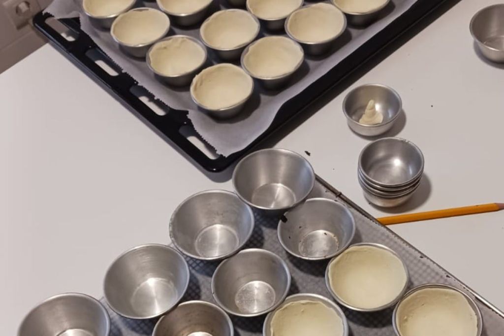 금속 베이킹 몰드는 반죽으로 채워져 양피지가 깔린 베이킹 트레이에 놓여 있습니다. 사용하지 않은 금형이 근처에 있습니다.